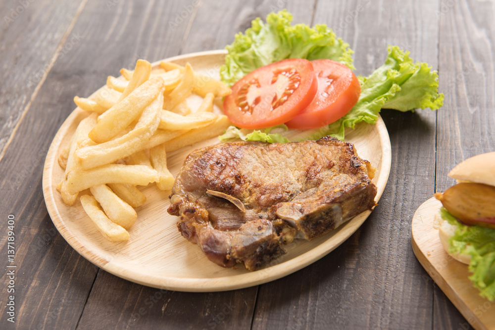 grilled pork chop steak and vegetables with french fries on wooden background grilled pork chop steak and vegetables with french fries on wooden background