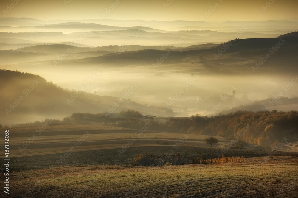 Fototapeta premium Misty morning landscape. Fog and hills in sunrise light, natural scenery