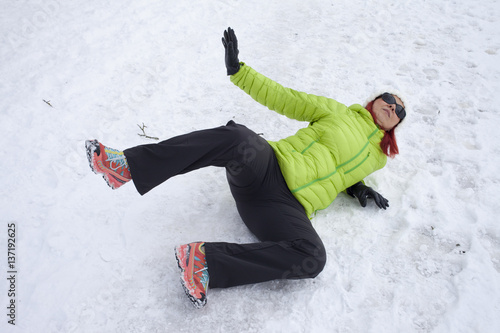 Risk of accidents in winter. Mid aged woman is slipping and falling on footpath, street covered with snow and black ice