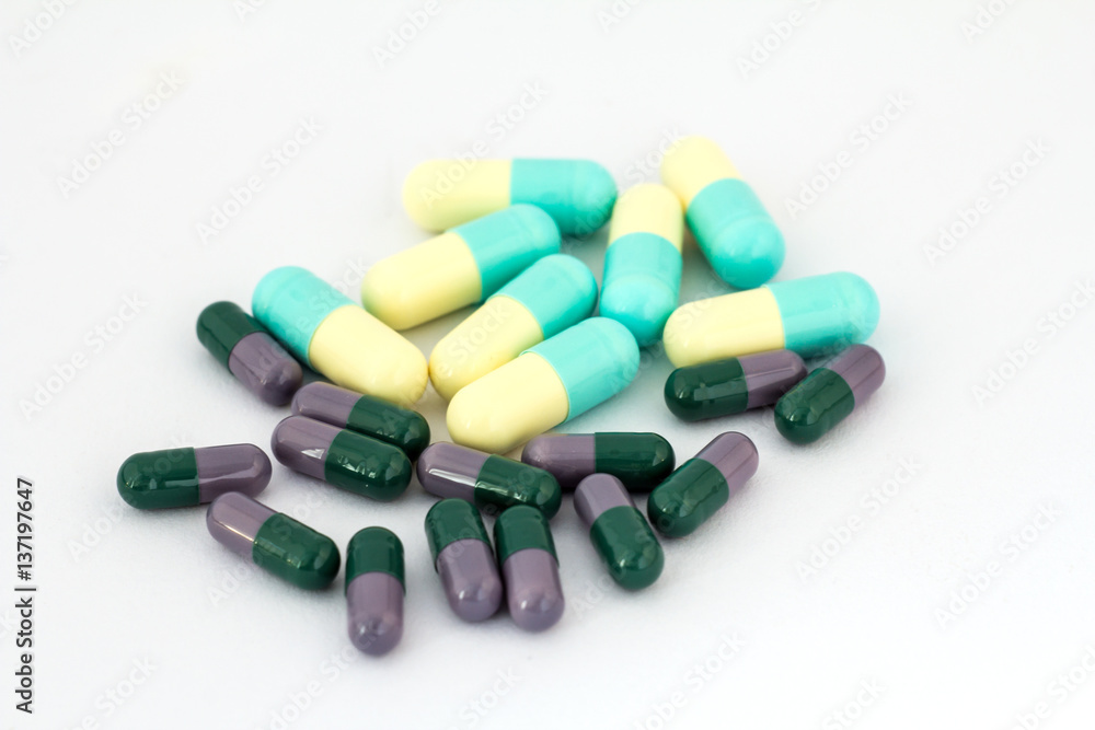 Pile of different pills on white backgroundg. Dark green and lilac, light yellow and blue capsules