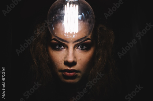 Mysterious photo of woman with light bulb. Portrait in the dark. Dangerous girl.