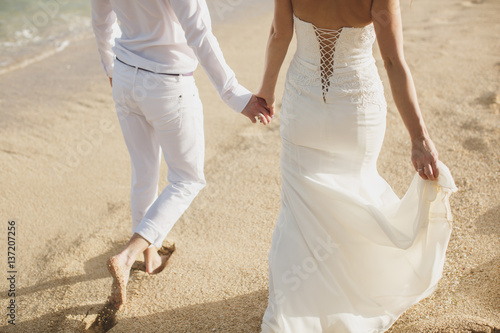 The bride and groom walk hand in the sand. footprints in the sand near the ocean