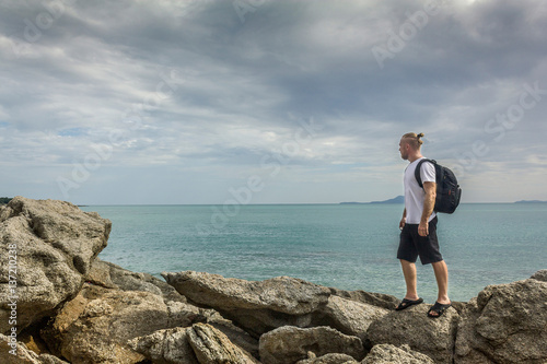 A person on stones near the ocean. A tourist standing on rocks and admiring waterscape. Horizontal outdoors shot. 