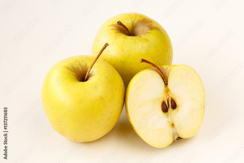 Half sliced and whole golden delicious apples on light beige background Half sliced and whole golden delicious apples on light beige background
