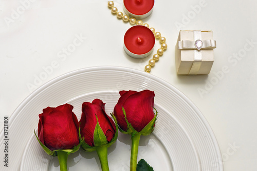 Red Roses on a white plate, candles and giftbox. Romantic composition for Val...