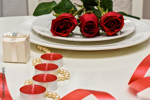 Red Roses on a white plate, candles and giftbox. Romantic composition for Val...