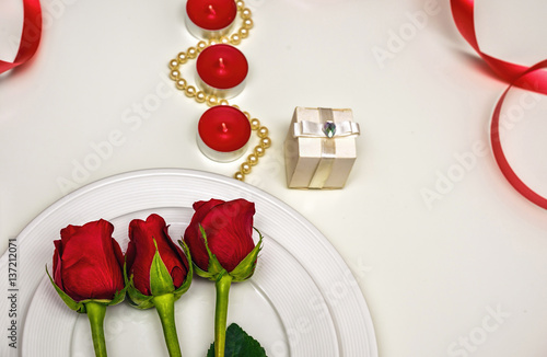 Red Roses on a white plate, candles and giftbox. Romantic composition for Val...