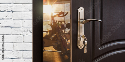 Entrance to gym in fitness club, opened door with exercise bikes © Prostock-studio