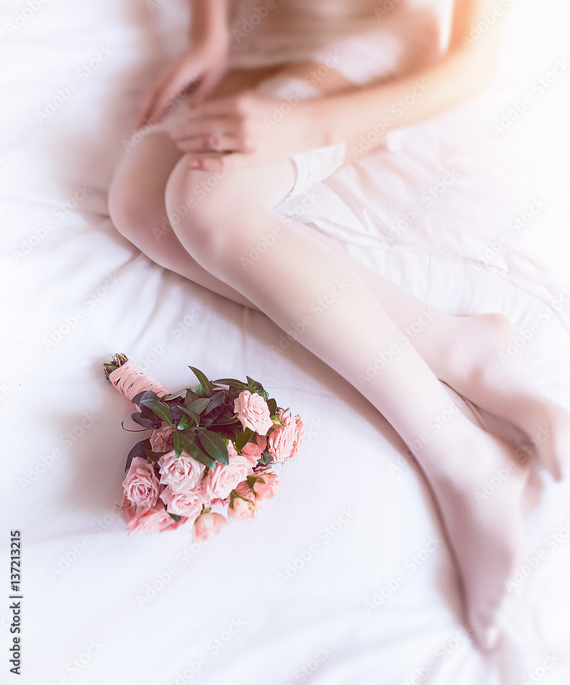 Tender pink bouquet lies before bride's knees on soft bed Tender pink bouquet lies before bride's knees on soft bed