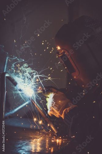 Metalwork industry background of man welding loops of steel pipe, generating sparks, smoke and reflexions