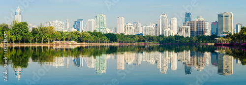 panorama of metropolis building with the green park and blue sky , the city park reflection from water in lake.