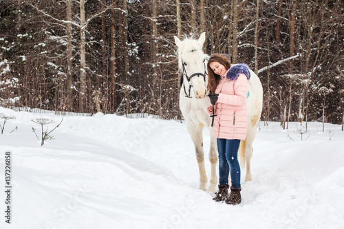 Nice girl and white horse outdoor in snowfall in a winter