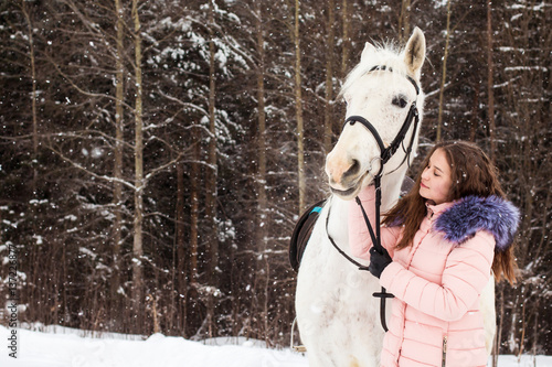 Nice girl and white horse outdoor in snowfall in a winter