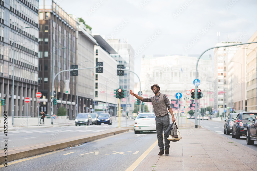 young handsome afro black man trying to call a taxi raising his hand in the city, overlooking left - transport concept