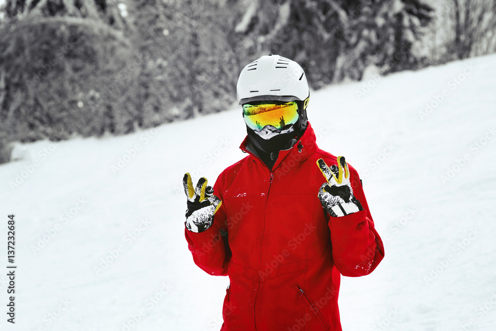 Snowboarder in red jacket, white helmet and yellow glasses poses on the hill