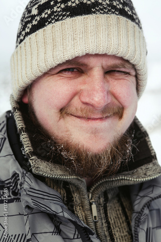 Funny bearded man in winter hat smiles standing outside