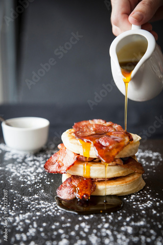 Female hand pouring maple syrup over breakfast bacon crumpet on slate
