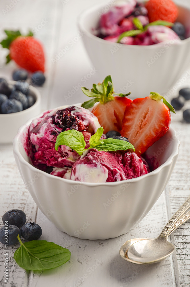 Ice cream with blueberries and strawberries in white bowl on white wooden background, selective focus Ice cream with blueberries and strawberries in white bowl on white wooden background, selective focus