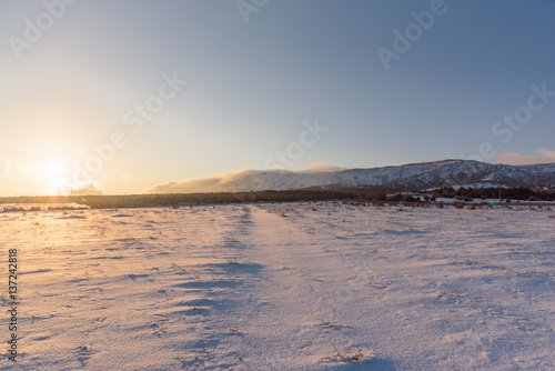 Winter road to the forest. Sunset landscape. Snow covered field.