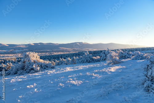 Sun shines on frozen forest and mountain with colorful sky