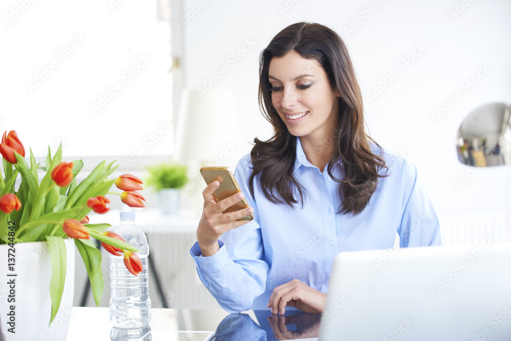 Trade and business. Shot of a young businesswoman send text message on her cellphone while sitting at office in front of laptop. Trade and business. Shot of a young businesswoman send text message on her cellphone while sitting at office in front of laptop.