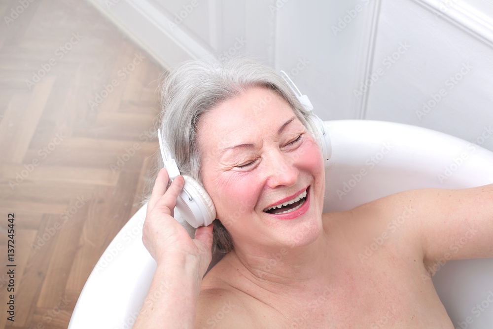 Senior woman smiling and listening to music in bath tub Photos | Adobe Stock