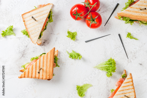 Club sandwiches with fresh lettuce, tomato, cucumber and salmon (trout). On crunchy toast. With ingredients on white concrete stone table top view copy space