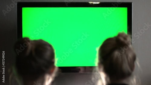Two young long-haired blond watching green TV screen and suddenly turn their heads together
