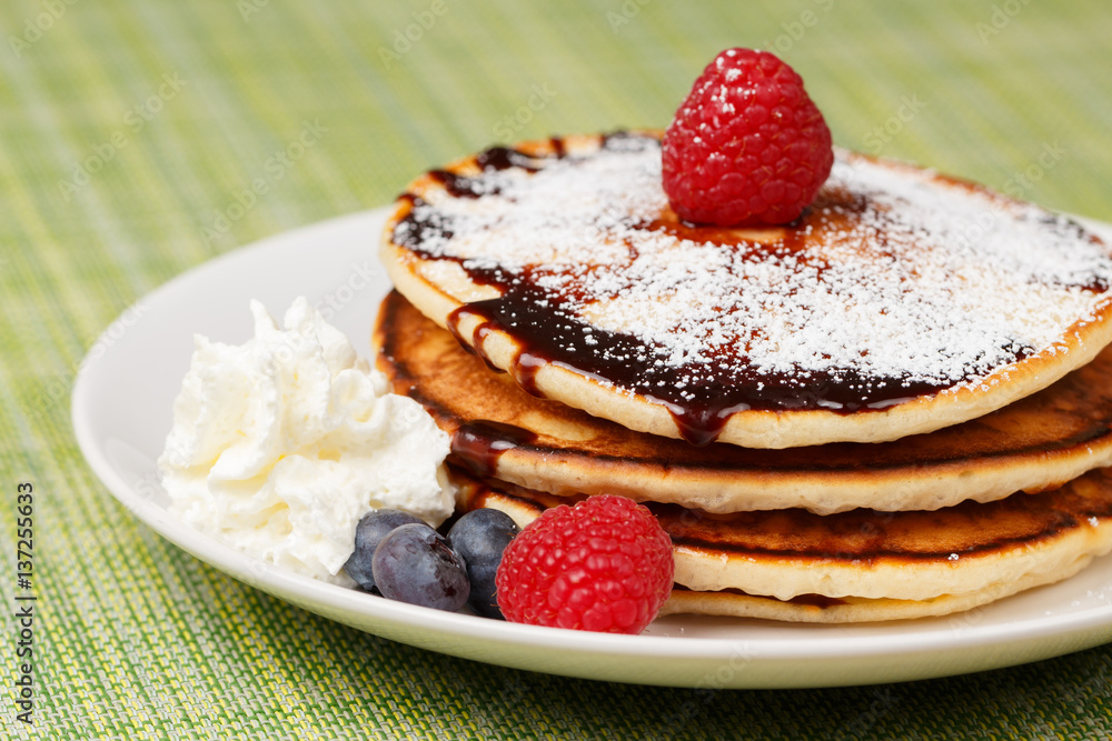 Pile of Pancakes with blueberries and raspberries, chocolate sauce and powder sugar Pile of Pancakes with blueberries and raspberries, chocolate sauce and powder sugar