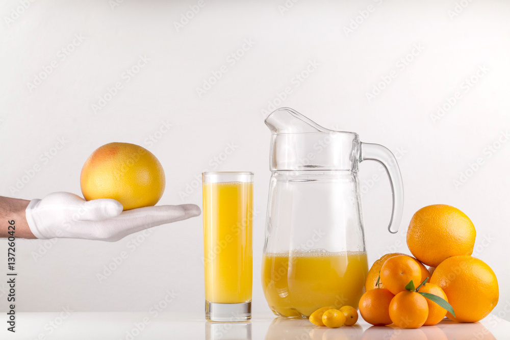 Hand holding an orange near the table with glass of orange juice and oranges