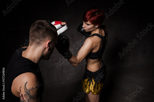 Tableau sur toile Woman boxer hitting training mitts held a boxing trainer in dark room