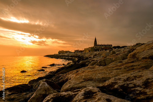 sunset on rock pier with church and calm sea