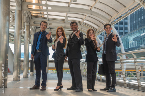 Business team standing together hand symbolize ok sign with in city.