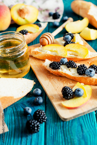 
sweet snack , bruschetta with berries and fruits , blueberries , blackberries and peaches , with butter and honey on wooden background