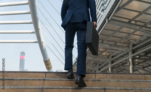 Rear businessman carrying a briefcase walking up the stairs in the city. © kaew6566