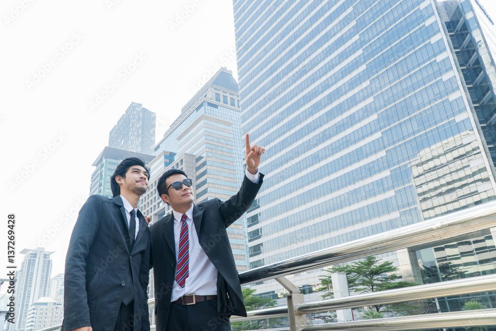 Two young businessmen talking and pointing at something while standing within the city. Two young businessmen talking and pointing at something while standing within the city.