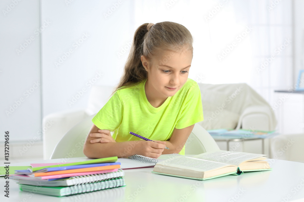 Attractive little girl sitting at table and doing home tasks Attractive little girl sitting at table and doing home tasks