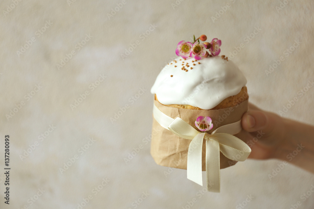 Hand holding Easter cake decorated with ribbon and flowers on light background Hand holding Easter cake decorated with ribbon and flowers on light background