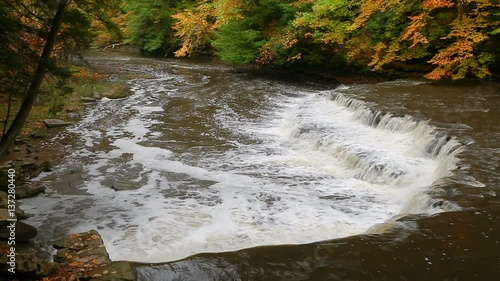 Seamless loop features whitewater splashing over a wide and curving waterfall in Cleveland, Ohio Metro Parks' South Chagrin Reservation in autumn.
