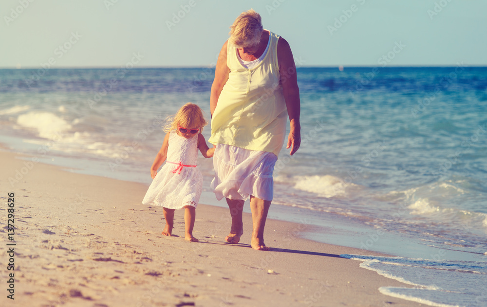 Happy grandmother with little granddaughter walk at beach