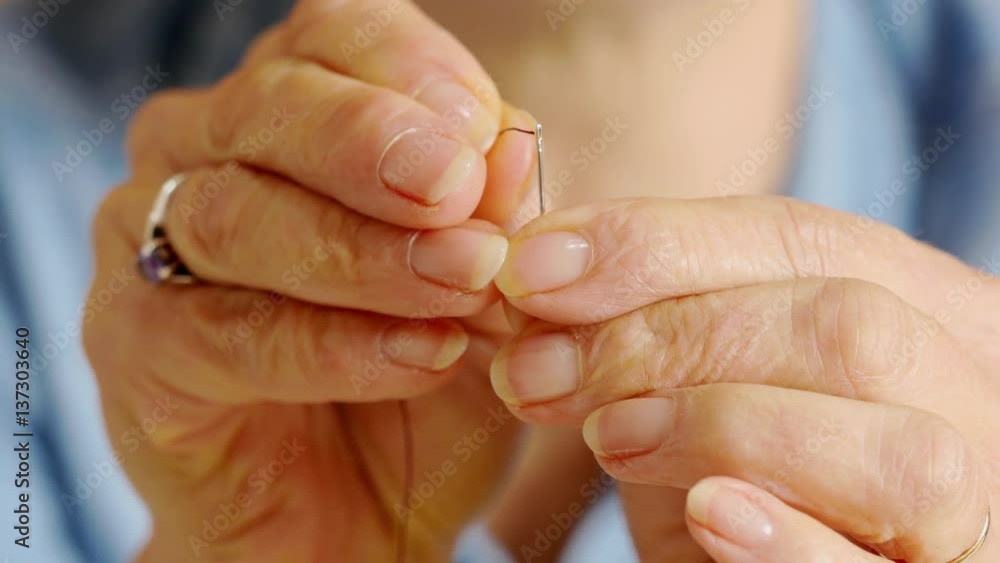 Macro of woman's fingers threading a needle Macro of woman's fingers threading a needle