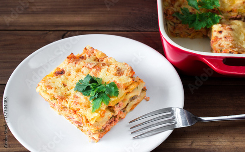 Close-up of a traditional lasagna topped with parskey leafs served on a white plate with fork