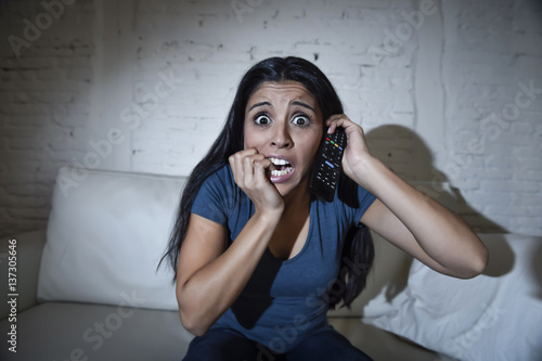 latin woman at home sofa couch in living room watching television scary horror movie or suspense thriller