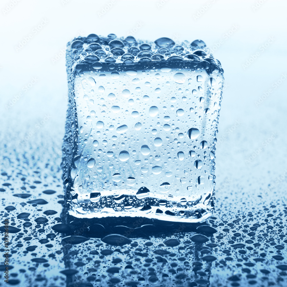 Transparent ice cube with reflection on blue glass with water drops Transparent ice cube with reflection on blue glass with water drops