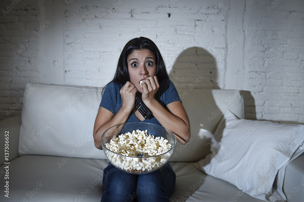 Naklejka premium latin woman at home sofa couch in living room watching tv covering eyes horrified