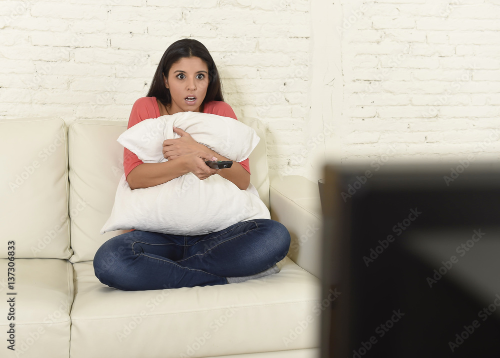 Naklejka premium latin woman sitting at home sofa couch in living room watching television scary horror movie