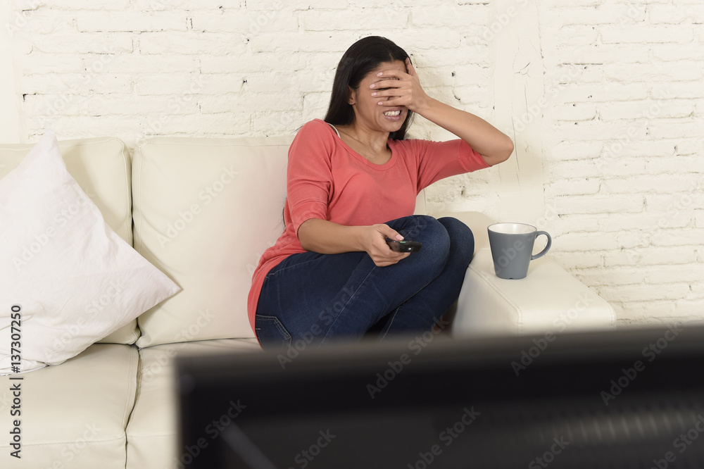 Naklejka premium latin woman sitting at home sofa couch in living room watching television scary horror movie