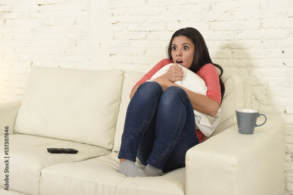 Naklejka premium latin woman sitting at home sofa couch in living room watching television scary horror movie
