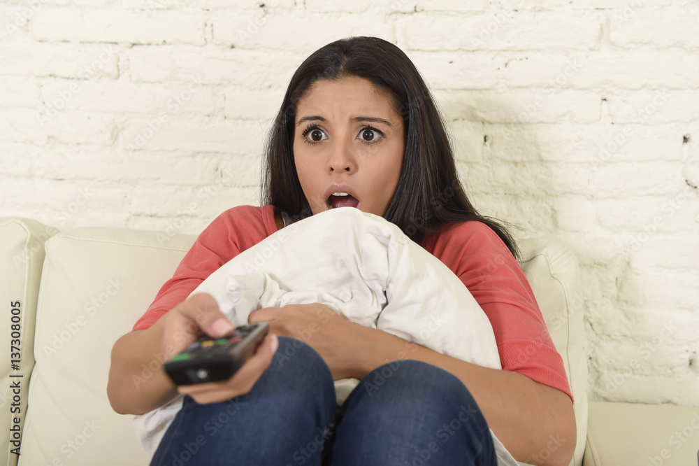 Naklejka premium latin woman sitting at home sofa couch in living room watching television scary horror movie