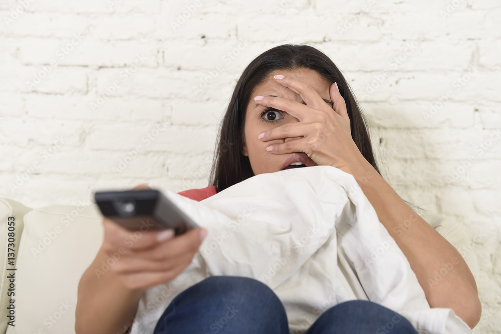 Naklejka premium latin woman sitting at home sofa couch in living room watching television scary horror movie